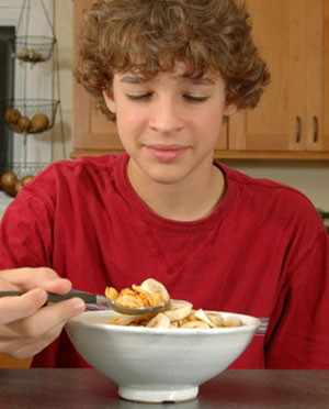 Boy eating a bowl of cereal with banana. 